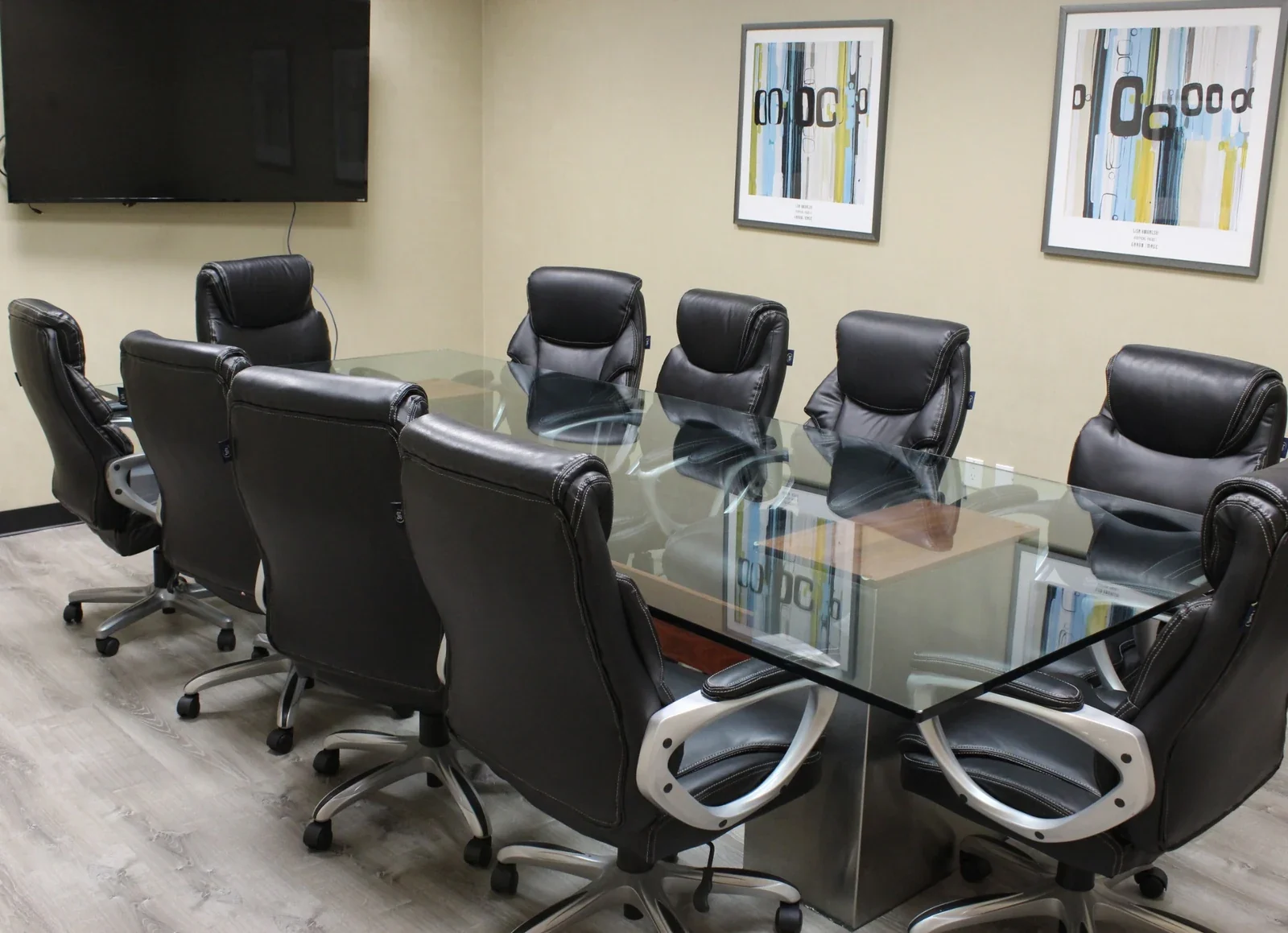 Large conference room with a glass table, black padded chairs and wall display.