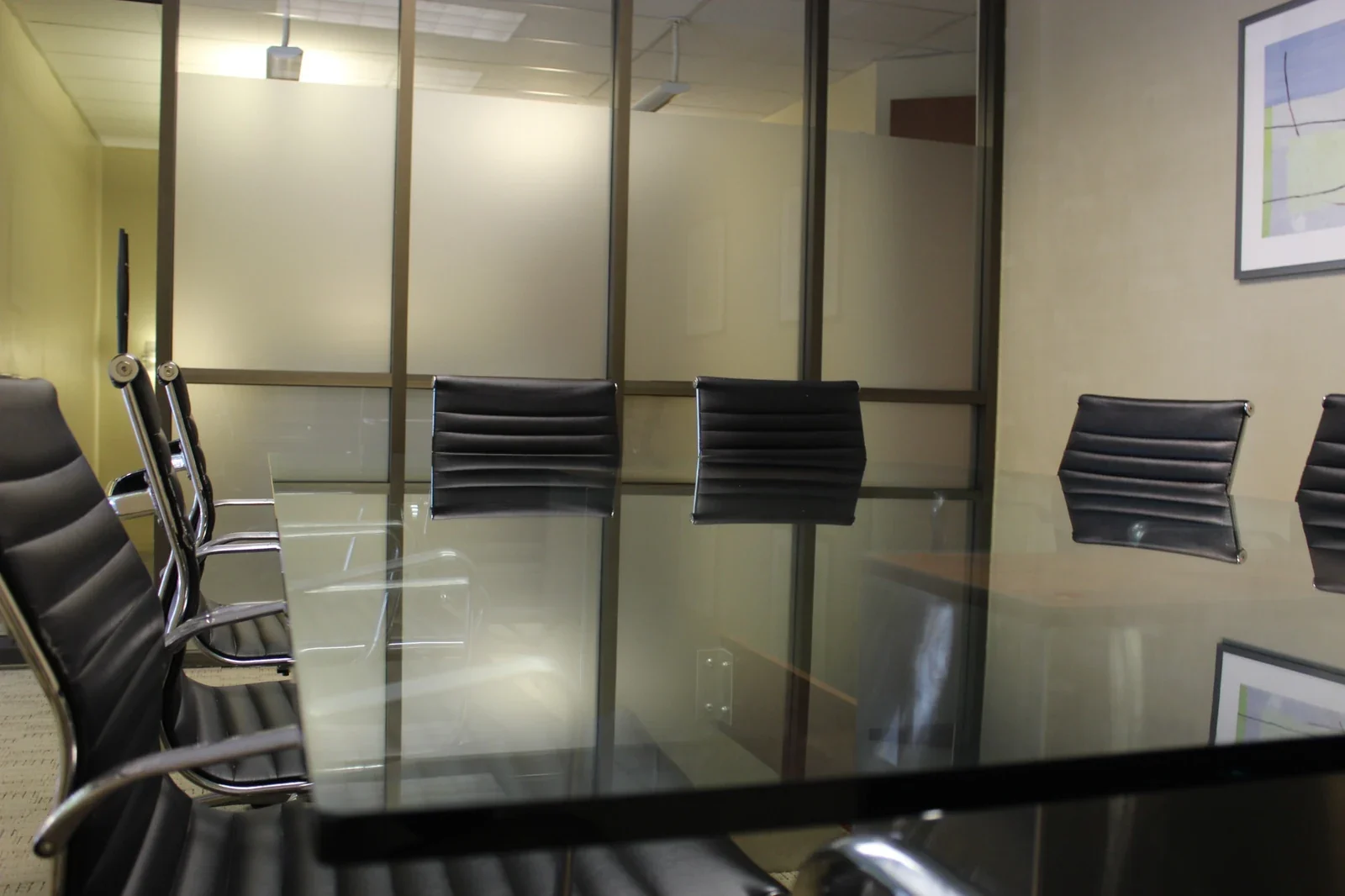 Glass meeting table with black ribbed chairs and frosted partitions.